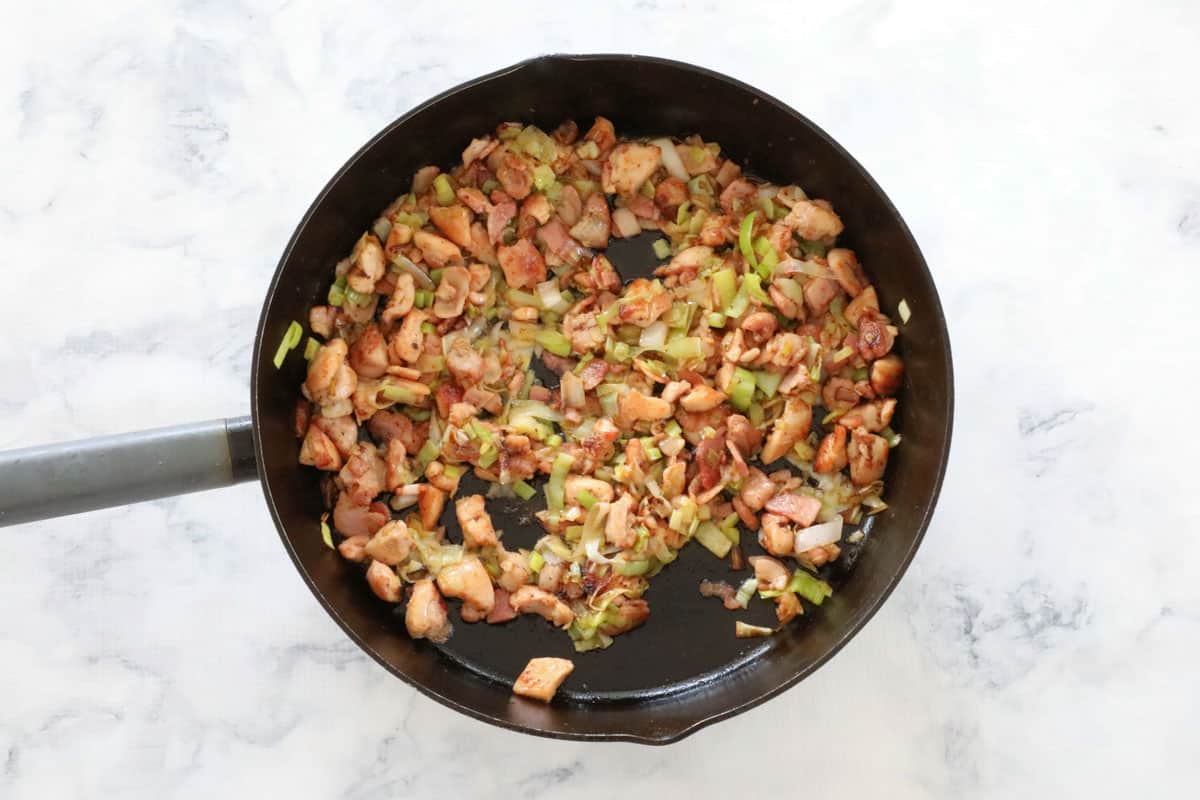 Softened leeks in a pan with chicken and bacon