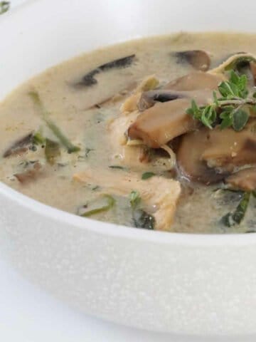 A bowl of mushroom soup with chicken and herbs.
