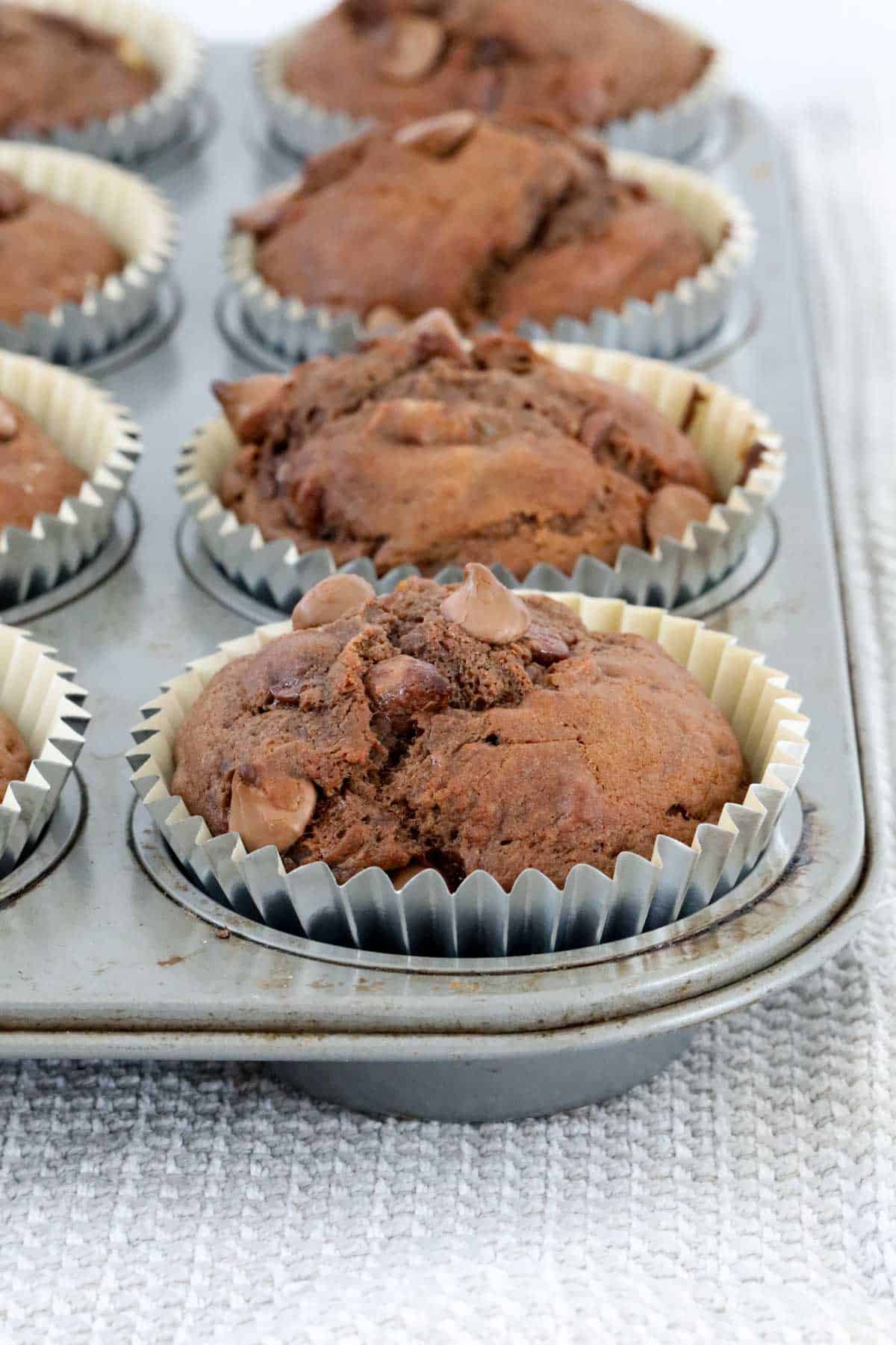 Silver muffin cases encasing chocolate banana muffins in a baking tray.