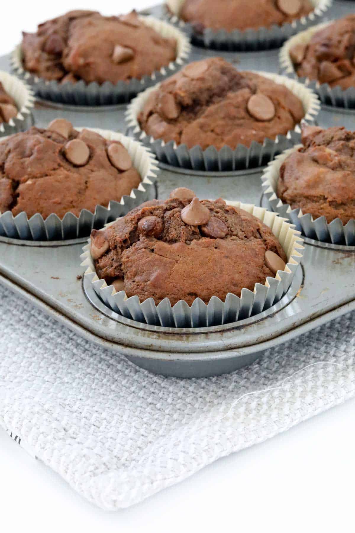 A muffin tray filled with chocolate banana muffins in silver cases.