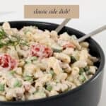 A black bowl filled with a creamy pasta salad with tuna.