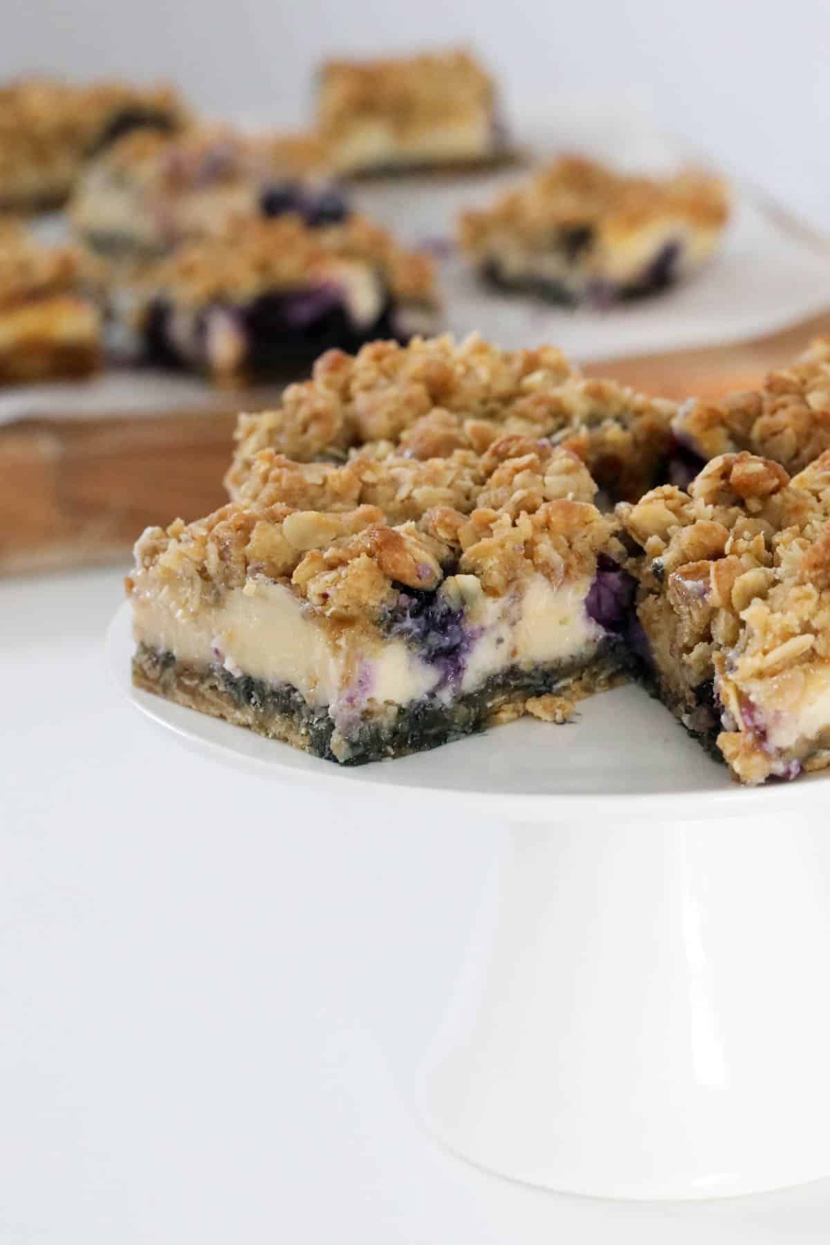 Pieces of blueberry crumble bars on a white cake stand.
