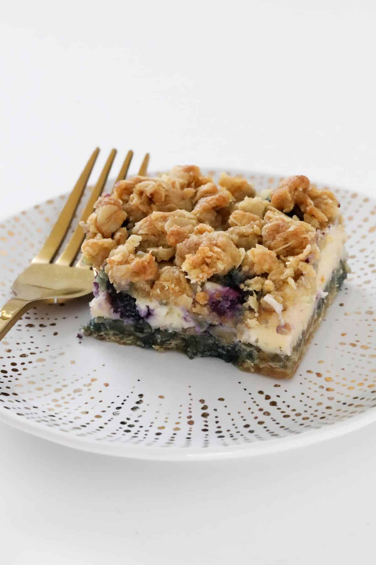 A piece of crumble slice on a white and gold plate with a gold fork resting on the plate next to it.