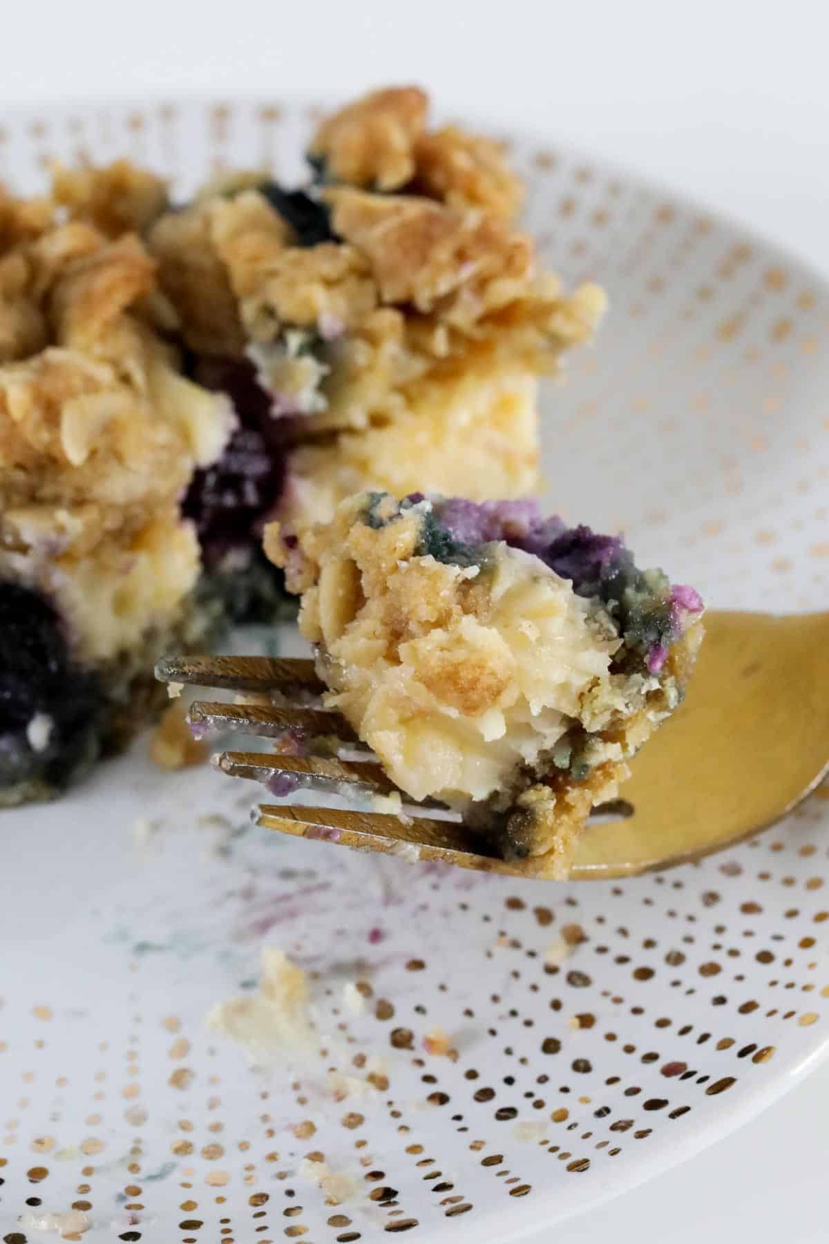 A gold fork with a creamy lemon and blueberry crumble bars on it.