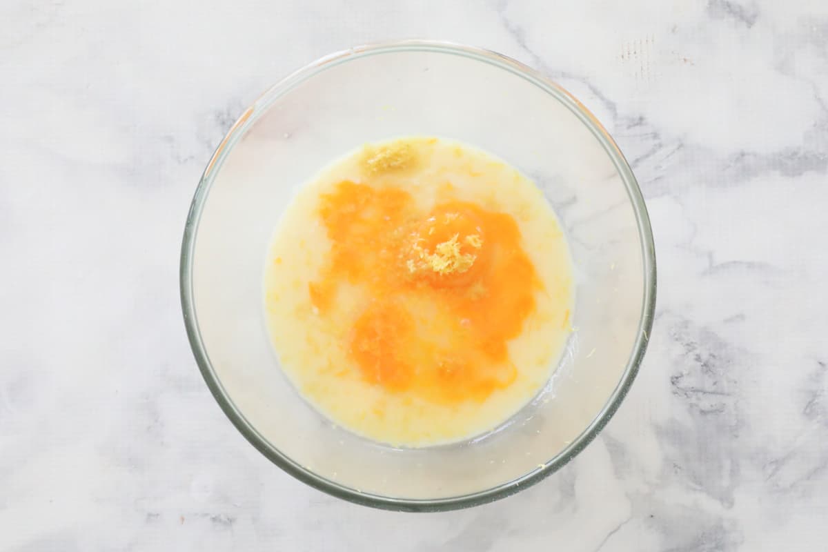 Eggs, condensed milk and lemon zest in a glass bowl.