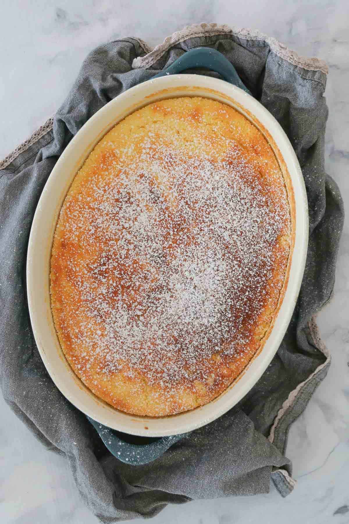 Looking down on a golden baked lemon delicious pudding, dusted with icing sugar.