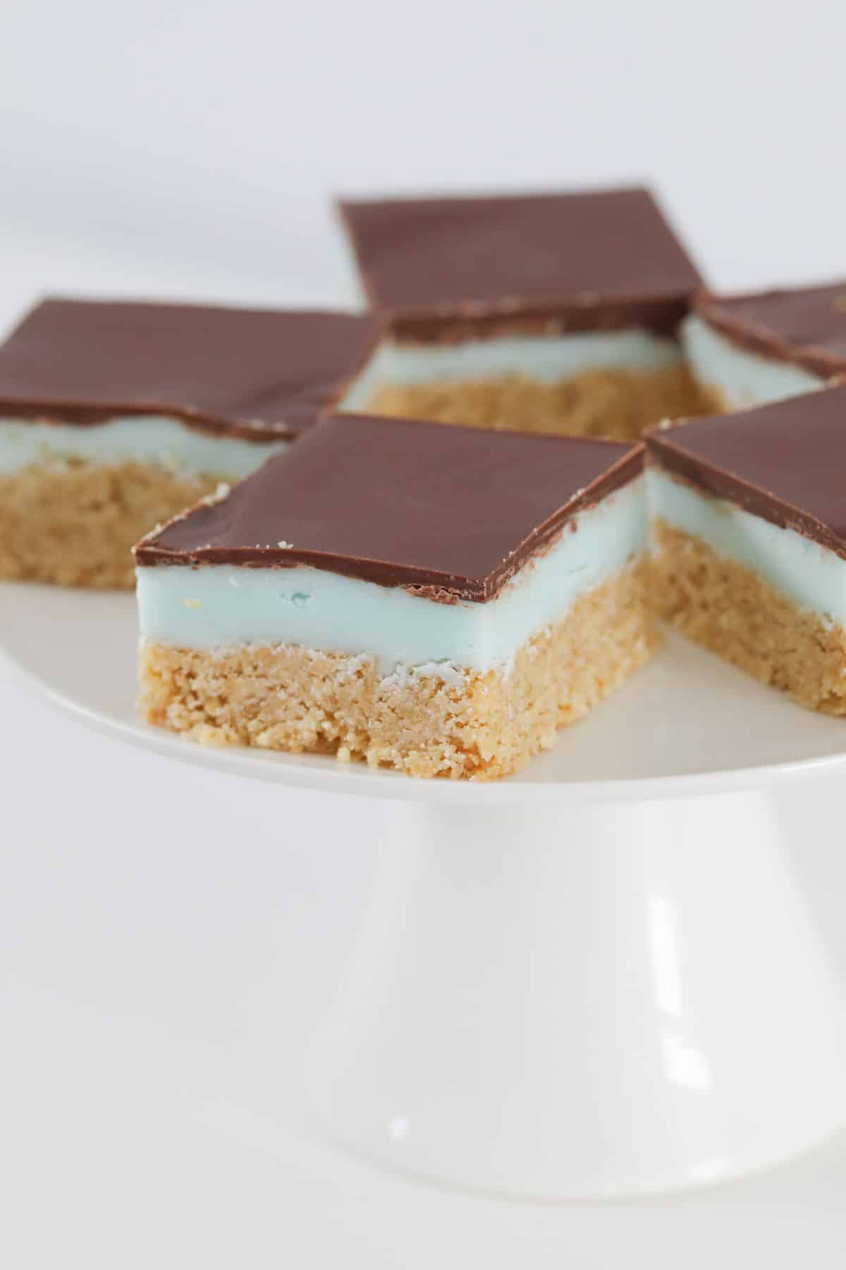 A white cake stand with traditional peppermint slice squares served on it.
