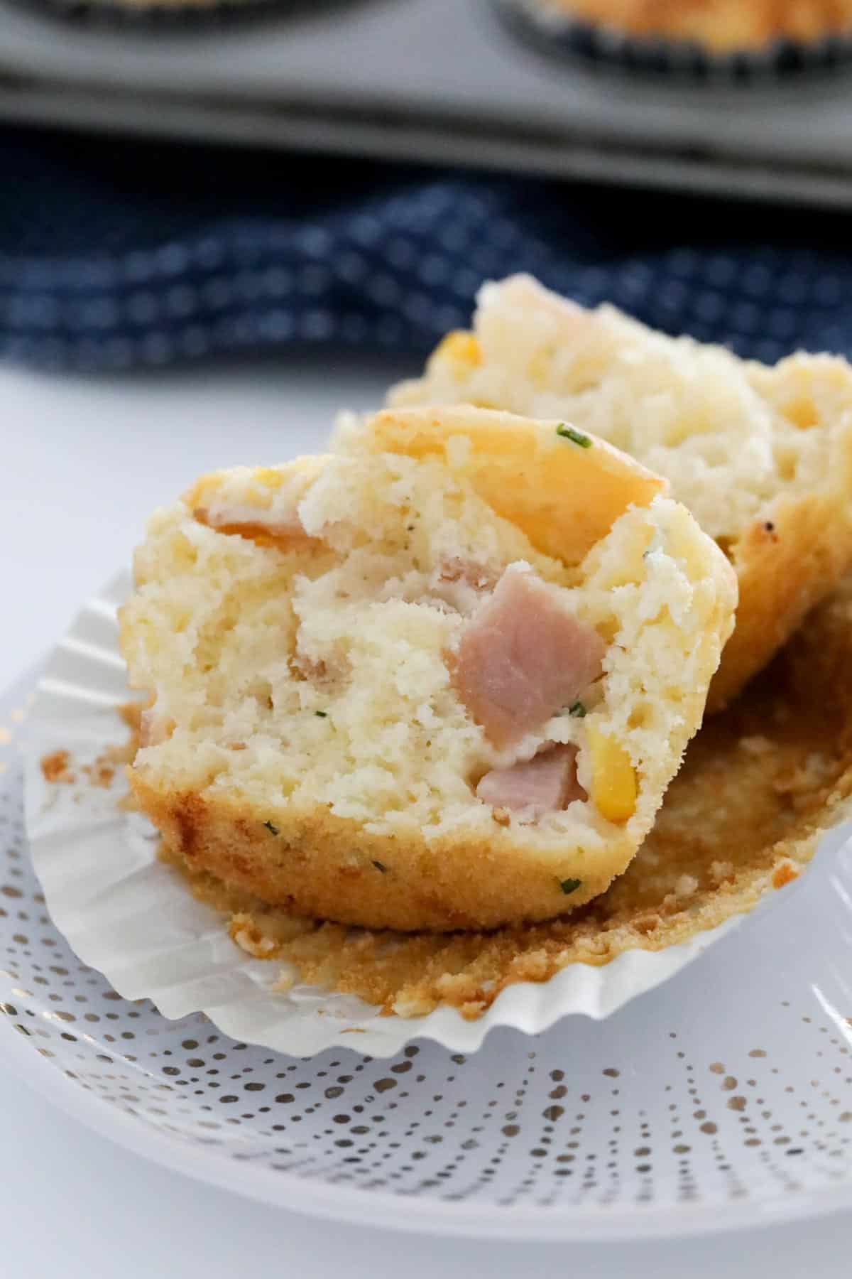 A muffin split open revealing pieces of ham and corn.