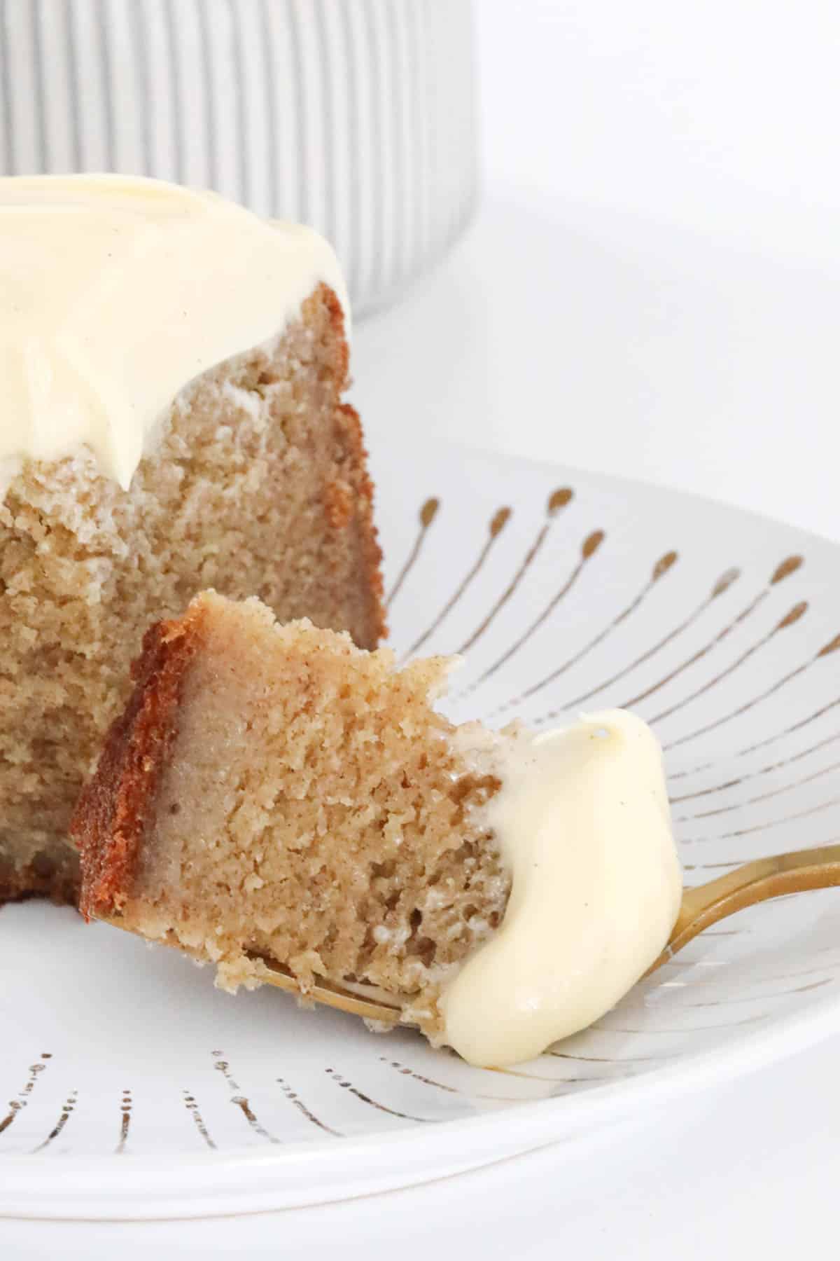 A gold patterned cake plate with a piece of frosted banana cake on a fork