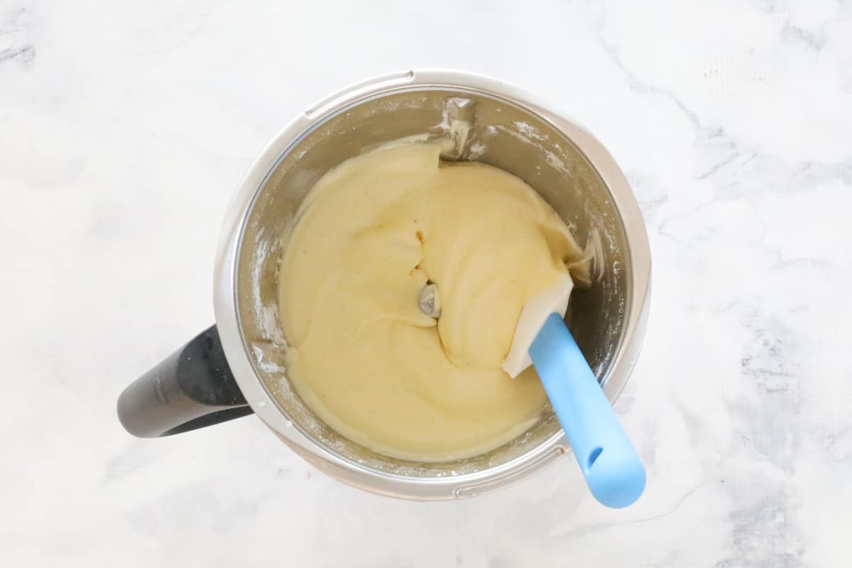 An overhead shot of a Thermomix bowl with a blue handled spatula resting in cake batter