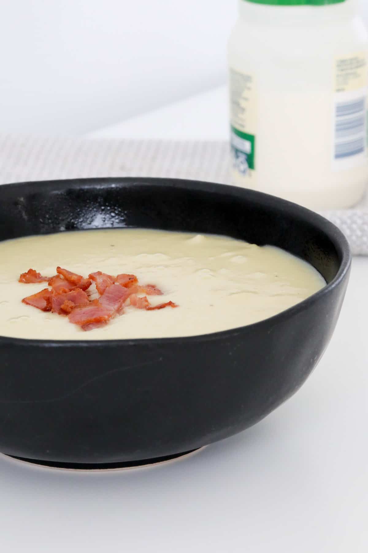 A black bowl filled with leek and potato soup with crispy bacon on top.