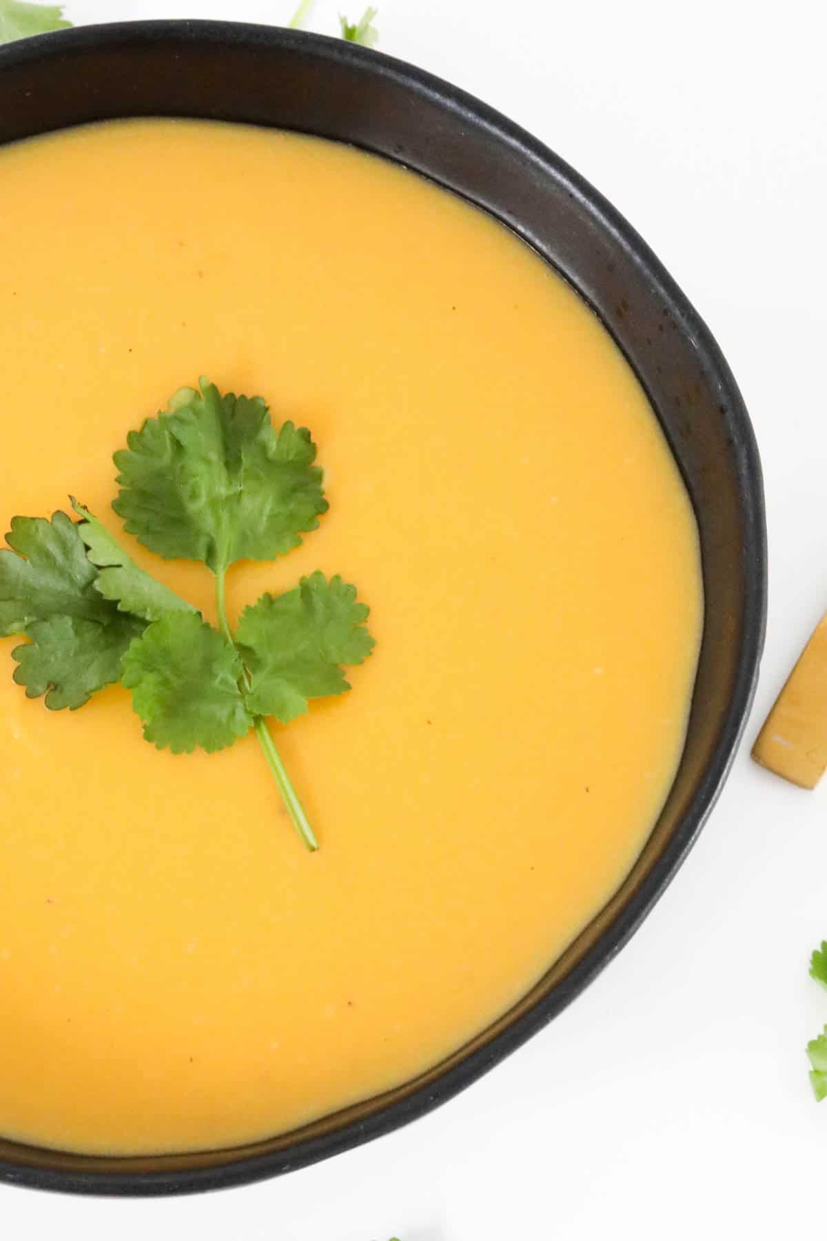 Bright yellow soup in a black bowl with a sprig of parsley on top