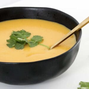 A golden spoon with Thermomix Pumpkin Soup lifted out of the black bowl beneath