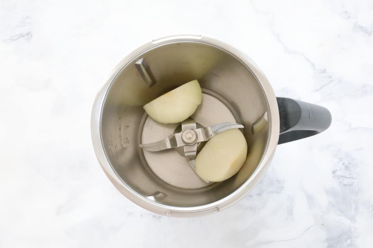 A halved brown onion in a Thermomix jug on a white marbled counter