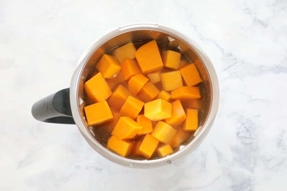 Raw pieces of pumpkin added to a Thermomix jug on a marbled countertop
