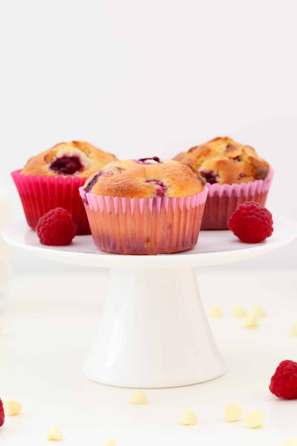 Three muffins in pink paper cases on a white cake stand.