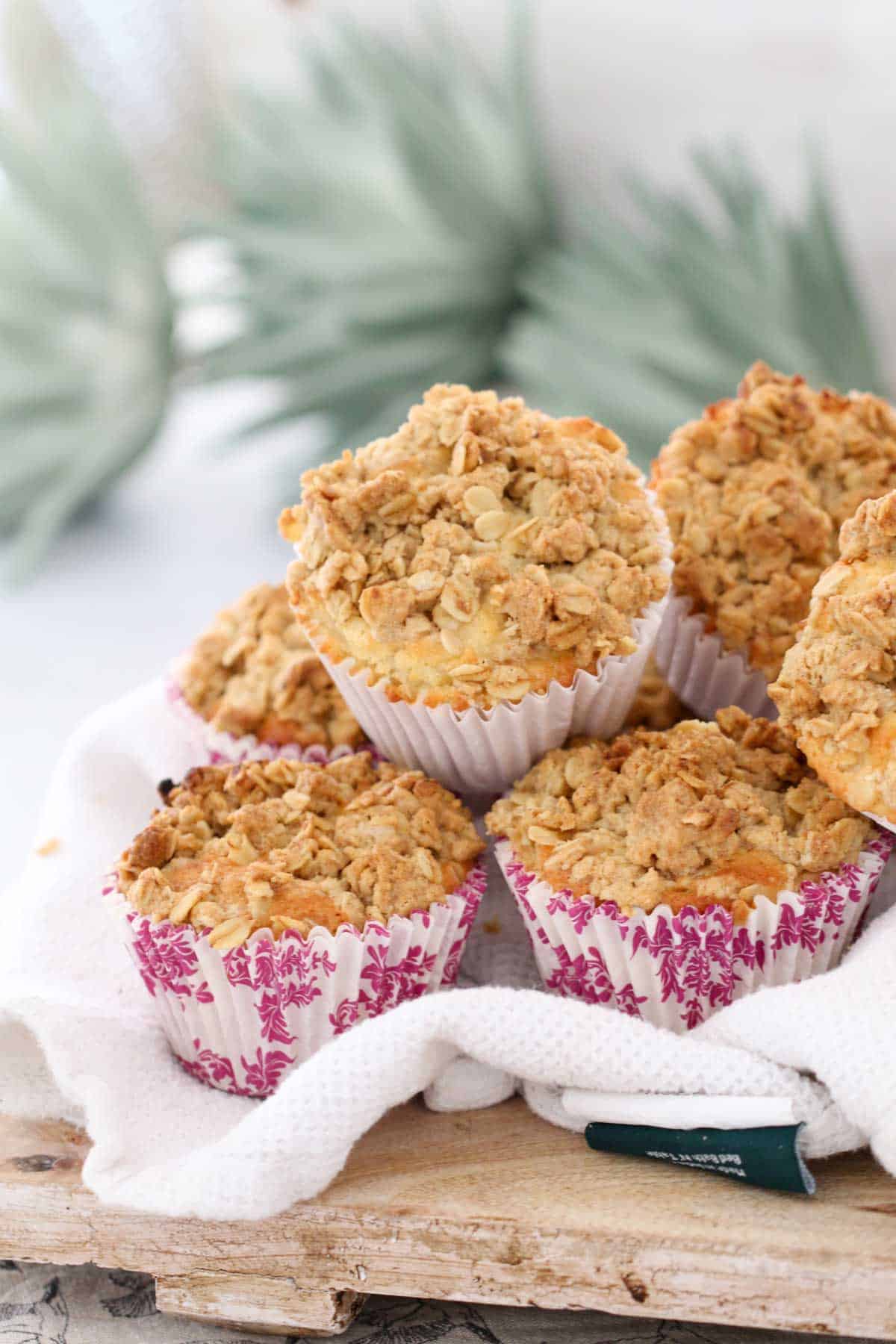 A pile of apple crumble muffins in pink and white paper cases on a wooden board.