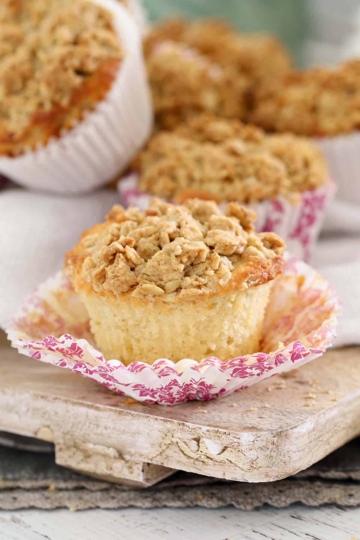 A muffin with a pink floral paper case opened on a wooden board.