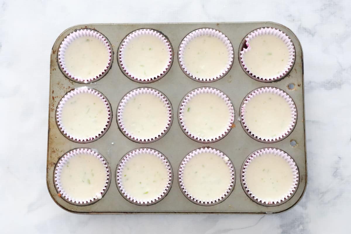 Muffin batter poured into paper cases in a muffin tray.