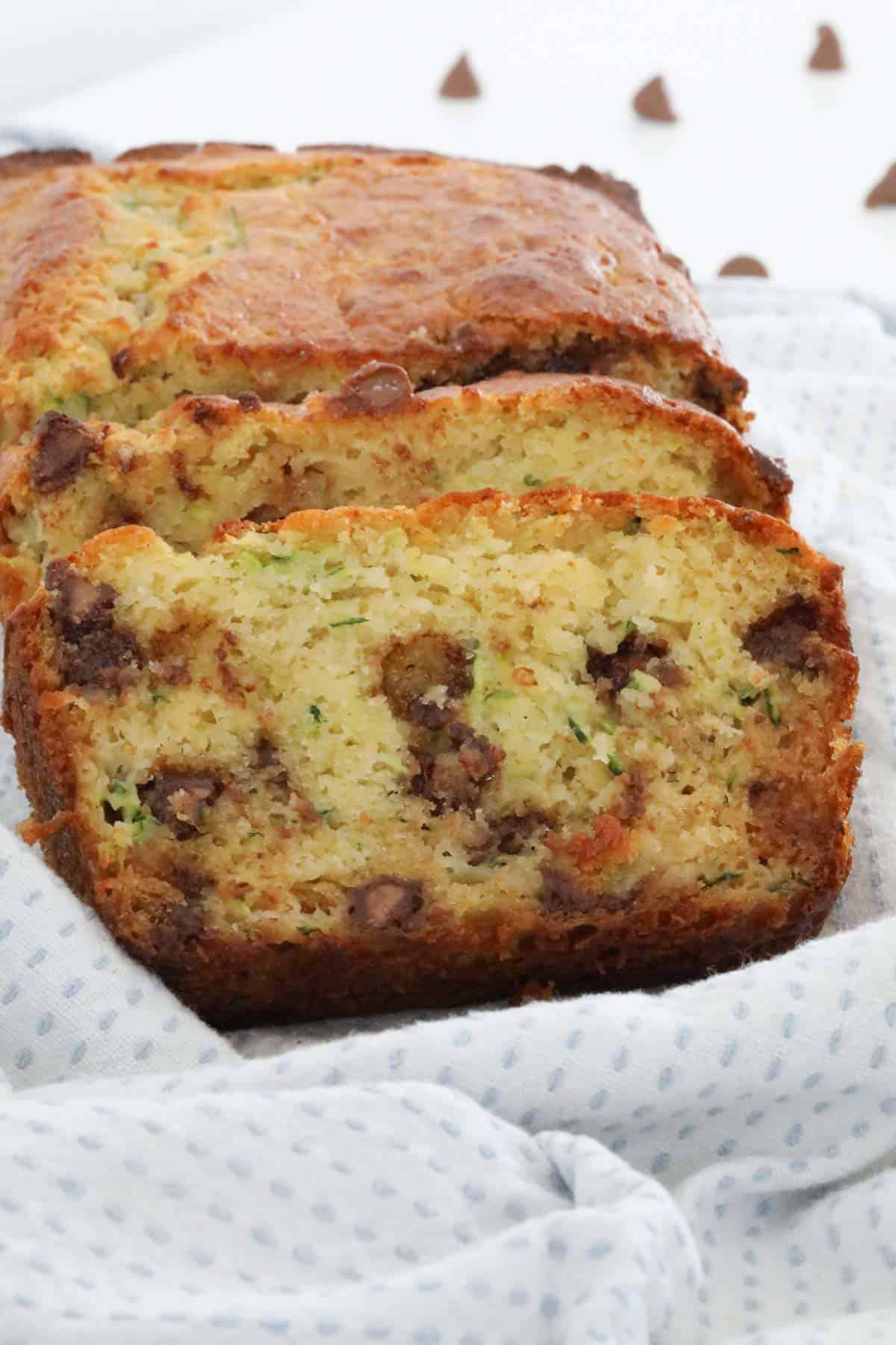 Slices of zucchini bread with chocolate chips on a tea towel.