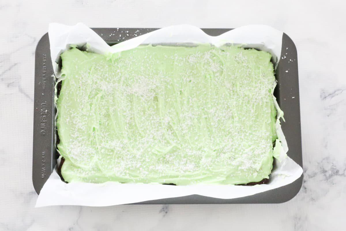 Minty icing spread over slice base in baking tray.