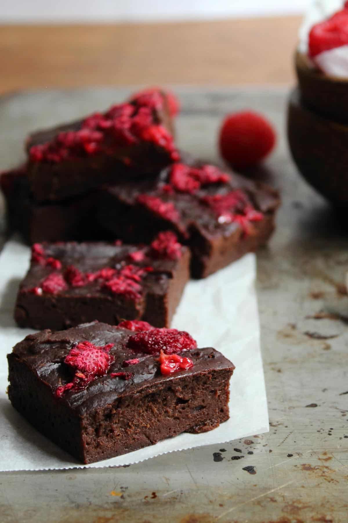 healthy chocolate brownies arranged on a baking tray with raspberries.