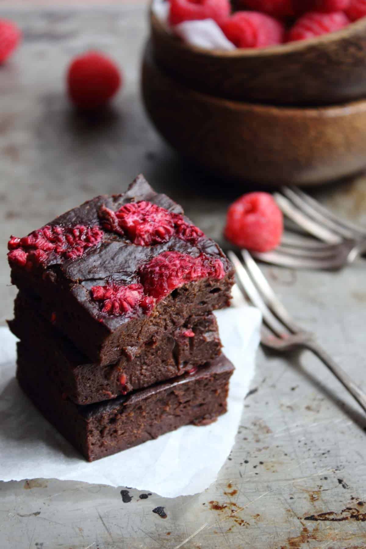chocolate brownies stacked on a baking tray with raspberries.
