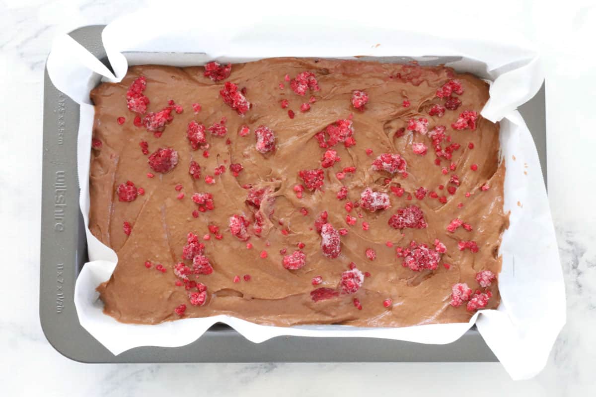 brownie batter topped with raspberries in a baking tin.