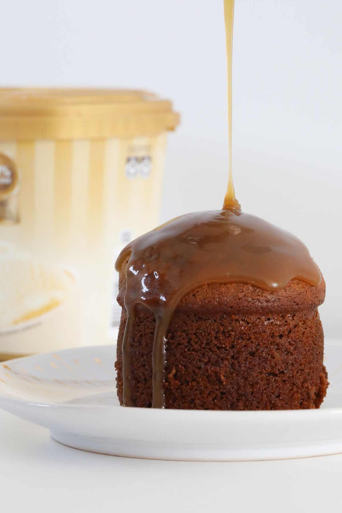 caramel sauce being poured over a mini sticky date pudding on a plate.