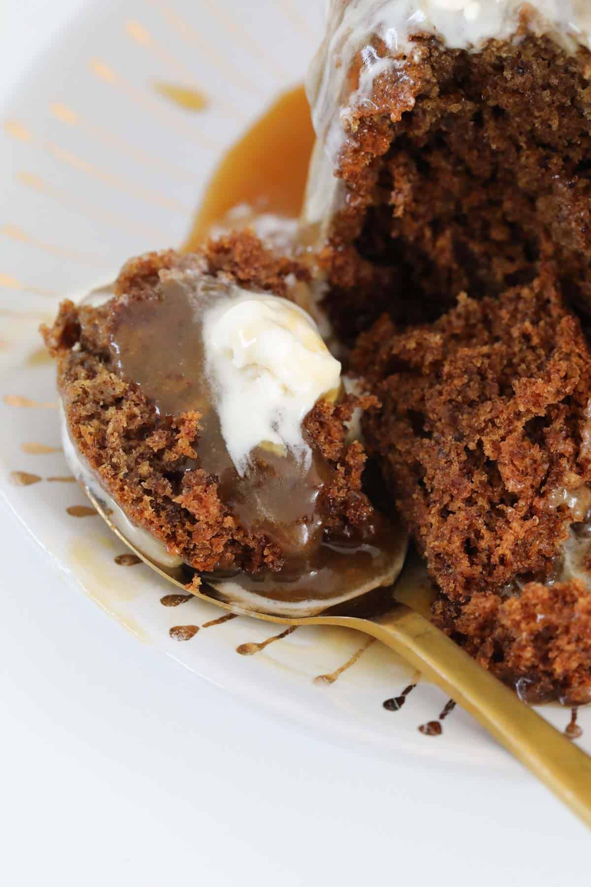 a spoon with sticky date pudding, caramel sauce and ice cream.