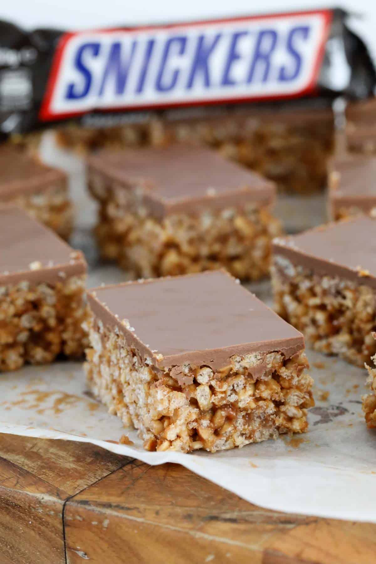 pieces of snickers slice topped with chocolate on a wooden board.