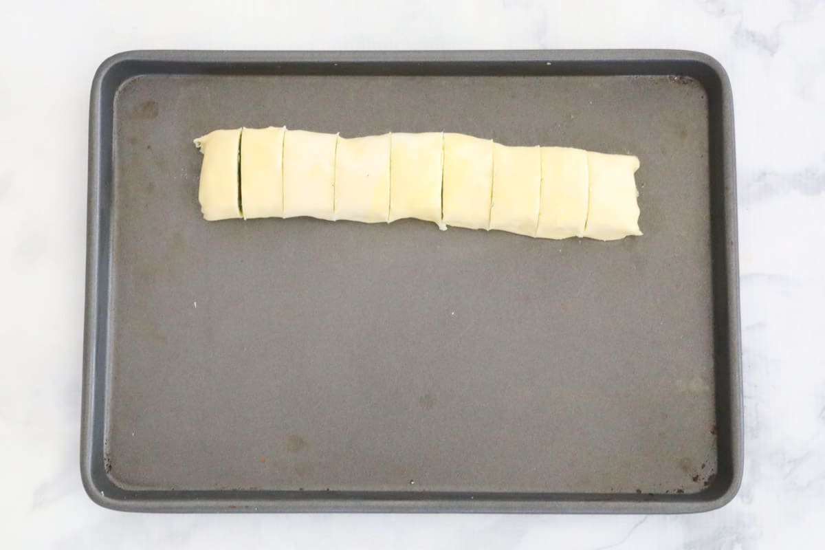 A puff pastry roll cut into pieces on a baking tray.