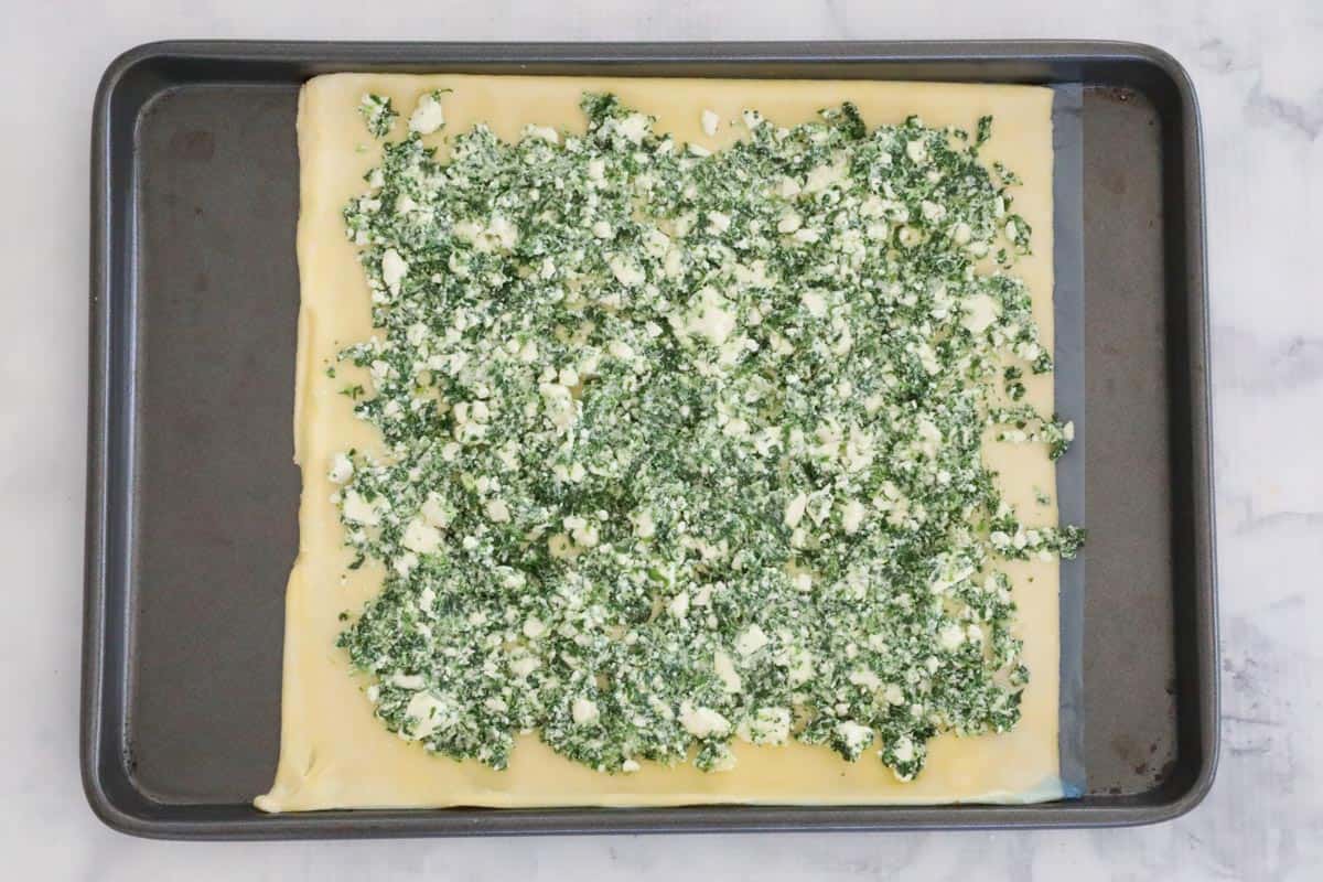 Puff pastry on a tray with spinach and feta filling spread over.