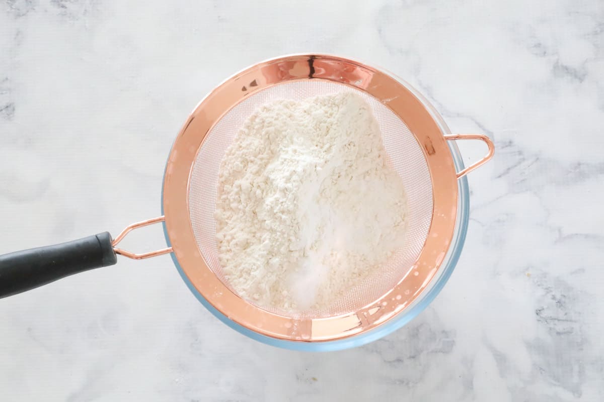 Flour being sifted into a glass mixing bowl.