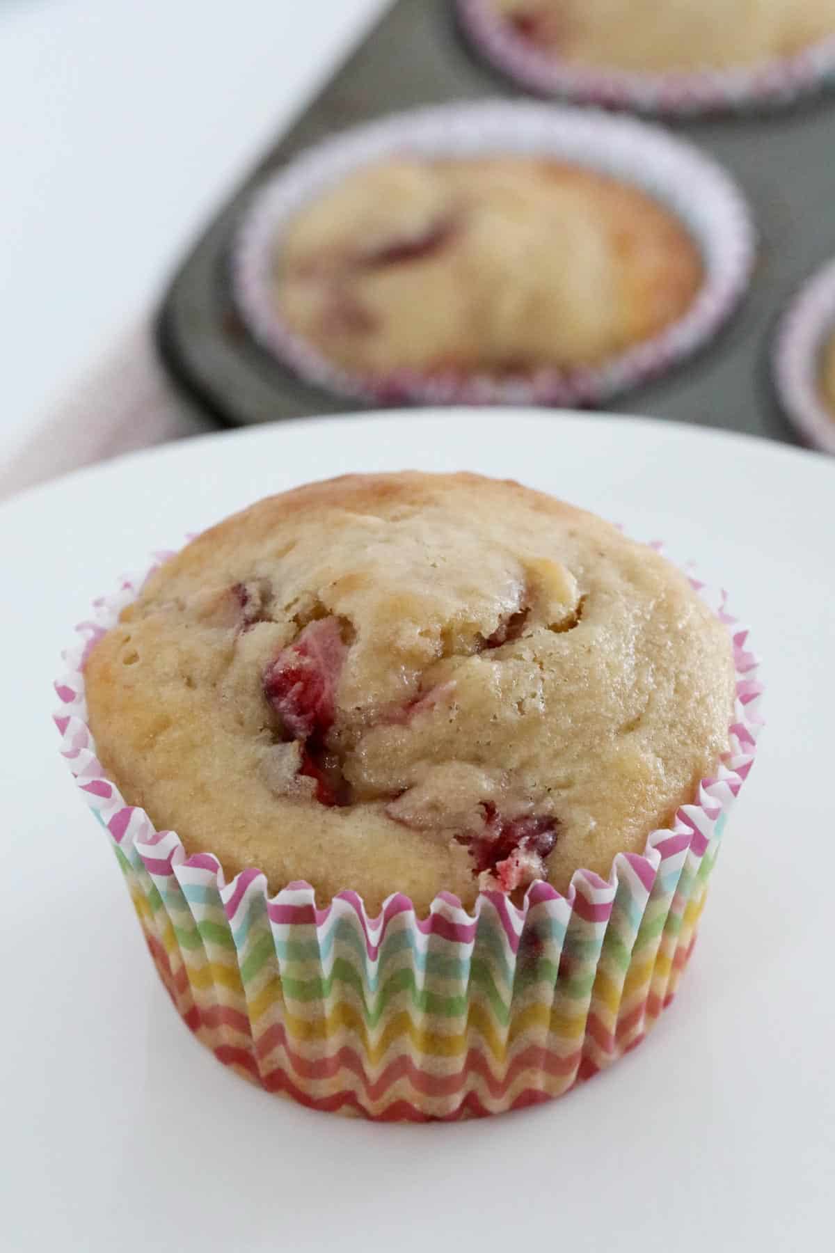 A banana muffin with strawberries in a colourful paper case on a white stand.