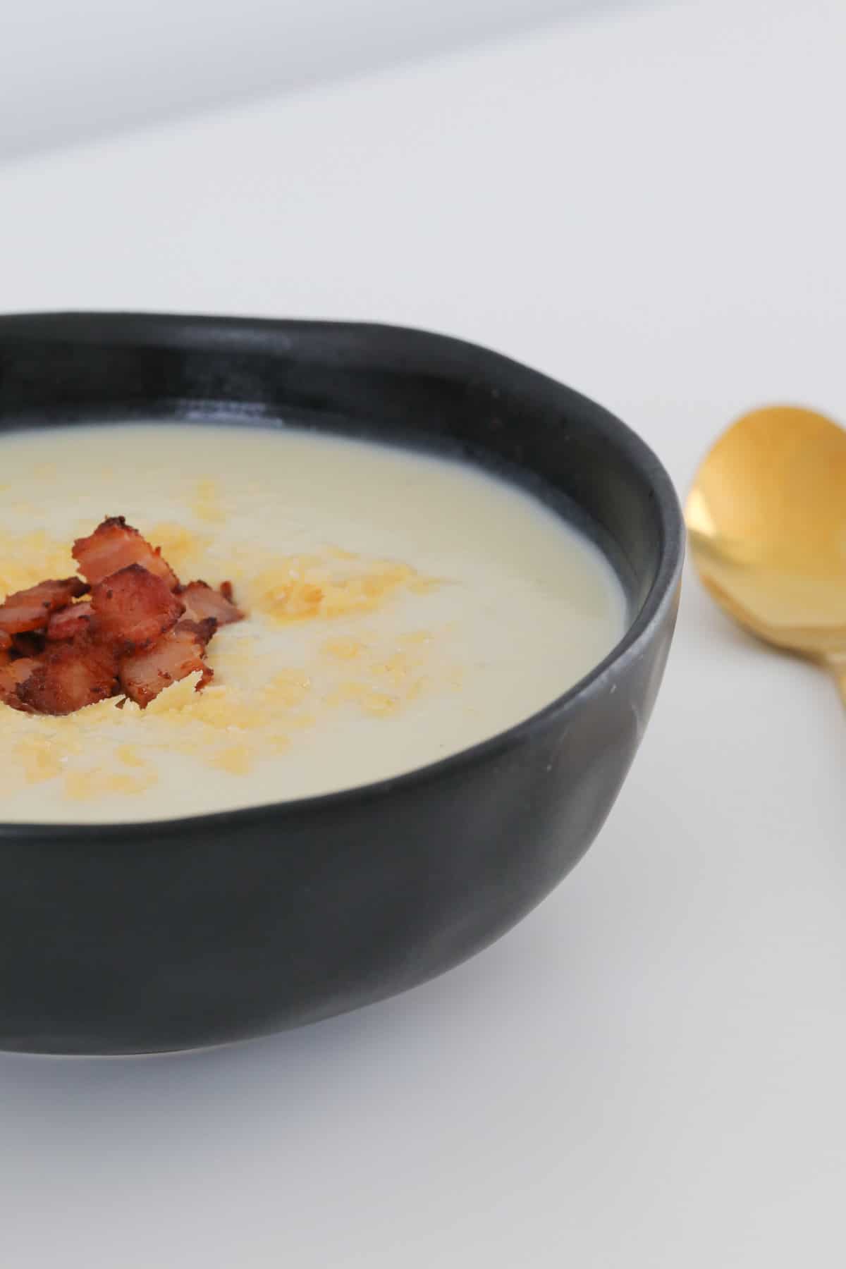 A side view of a white creamy soup with crispy bacon sprinkled on top, in a black bowl.