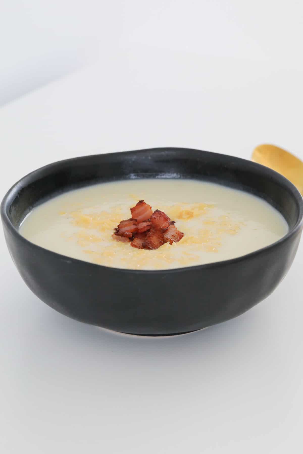 A rustic black bowl filled with creamy soup sprinkled with crispy bacon.