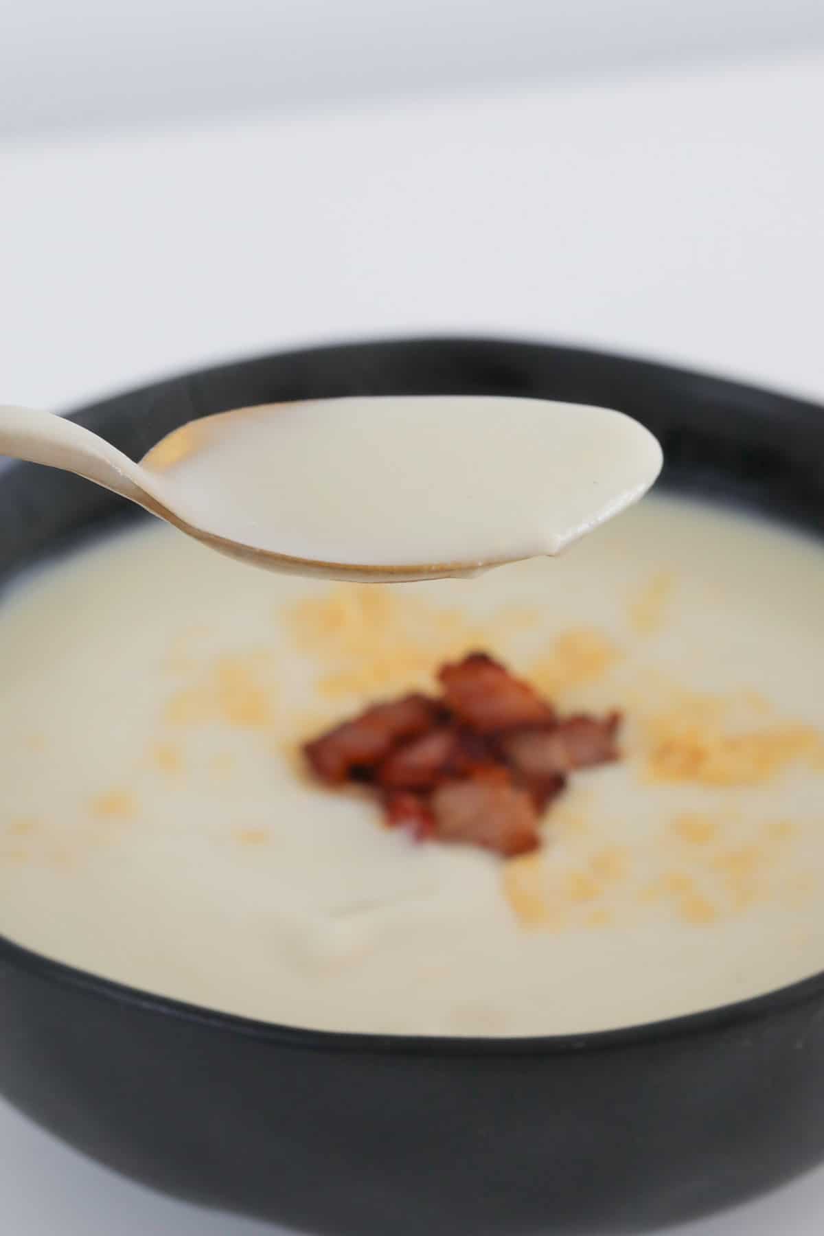 A spoonful of thick and creamy Thermomix Cauliflower Soup held above a bowl full of soup