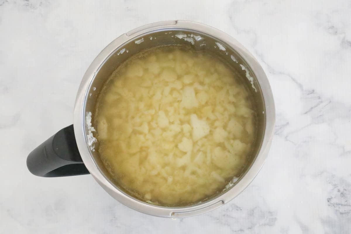 A Thermomix mixing bowl with stock liquid and pieces of cauliflower