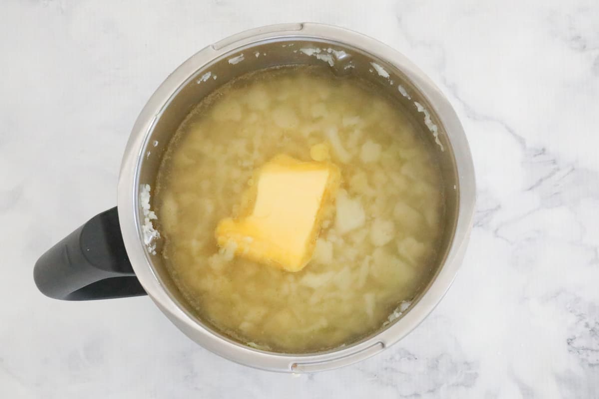 A chunk of butter melting into stock liquid with pieces of cauliflower in a Thermomix bowl