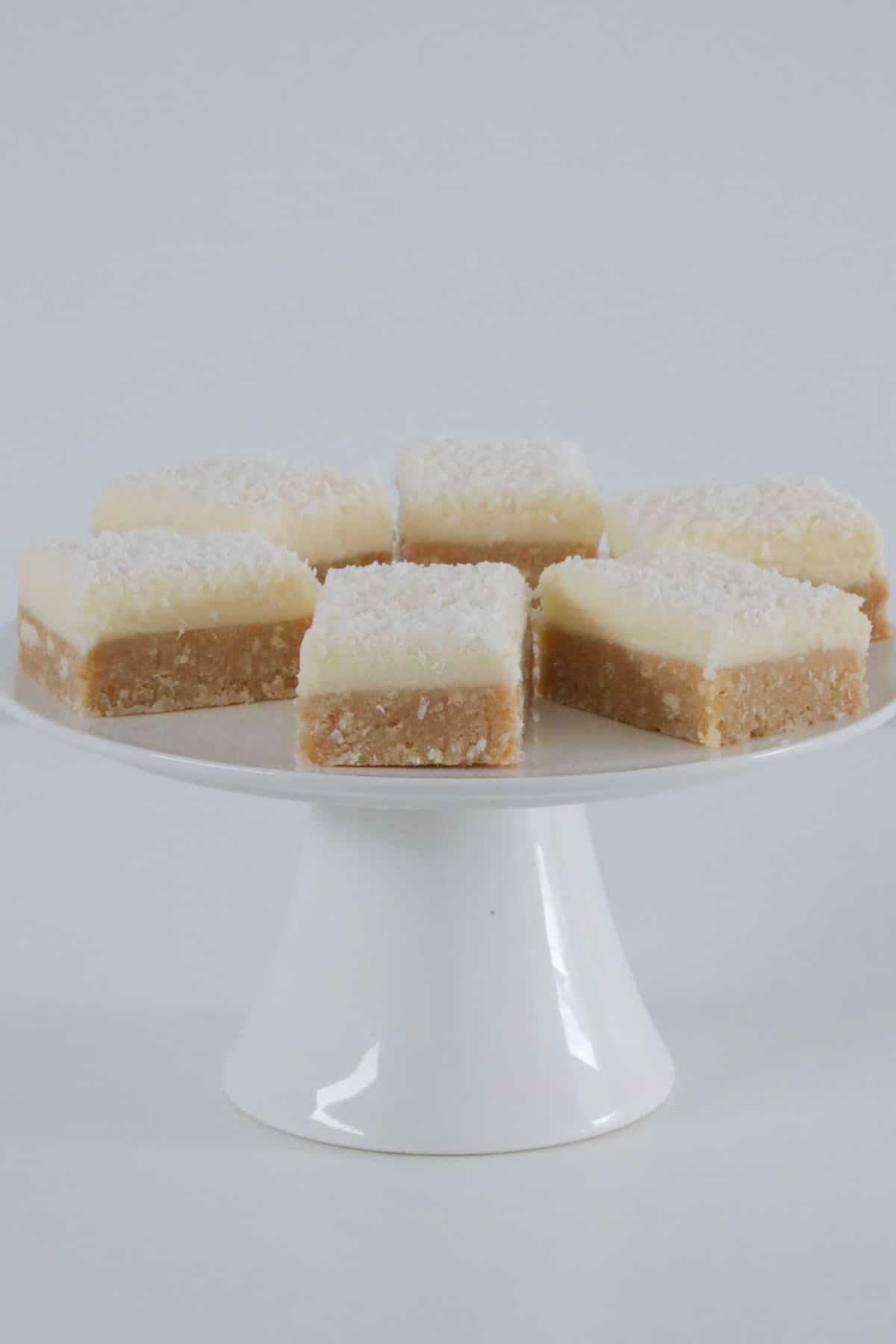 Pieces of lemon slice topped with frosting and coconut on a white cake stand.