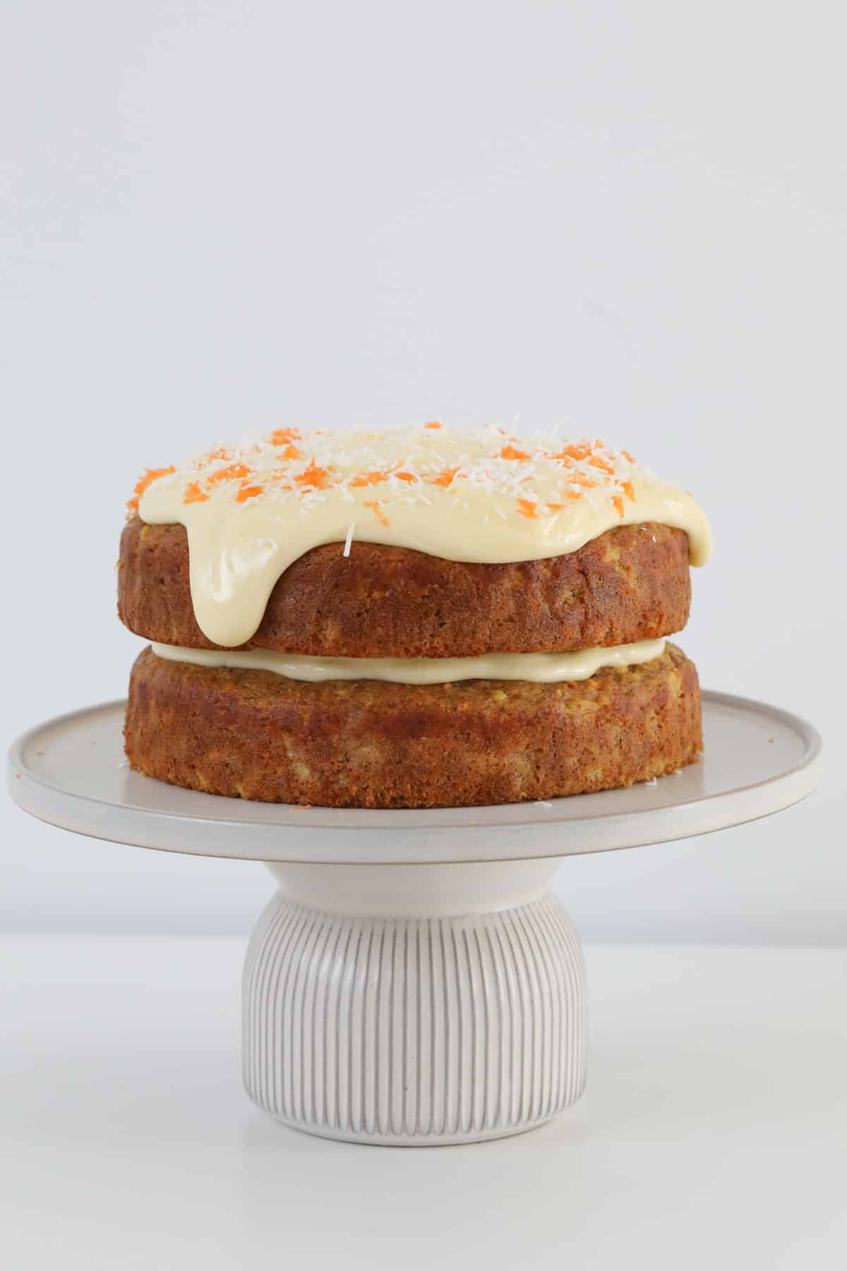 A layered carrot cake on a cake stand with cream cheese frosting.