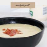 a black bowl filled with creamy potao & leek soup, and crispy bacon sprinkled on top.
