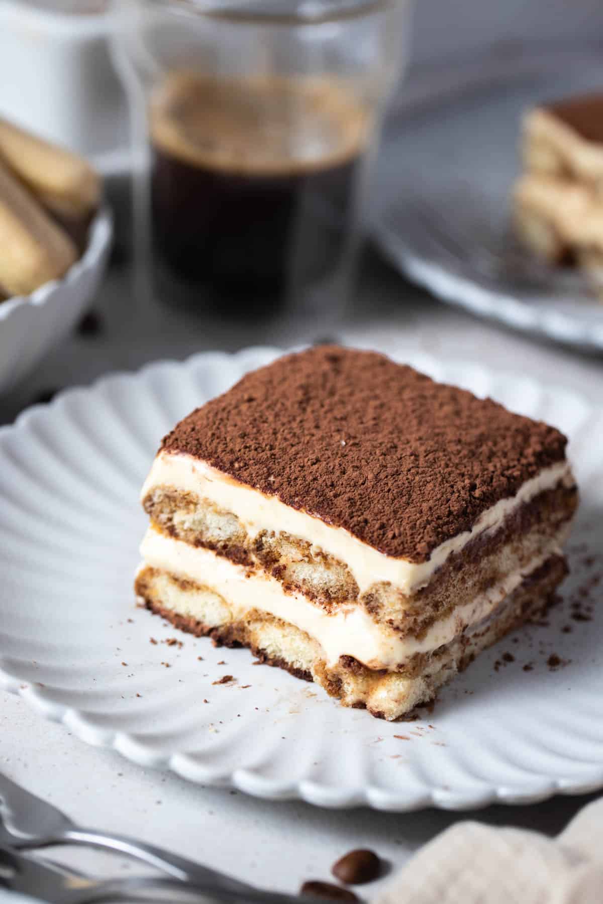 a slice of tiramisu on a white plate topped with cocoa powder.