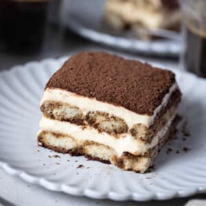 a piece of tiramisu topped with cocoa powder, on a white plate.