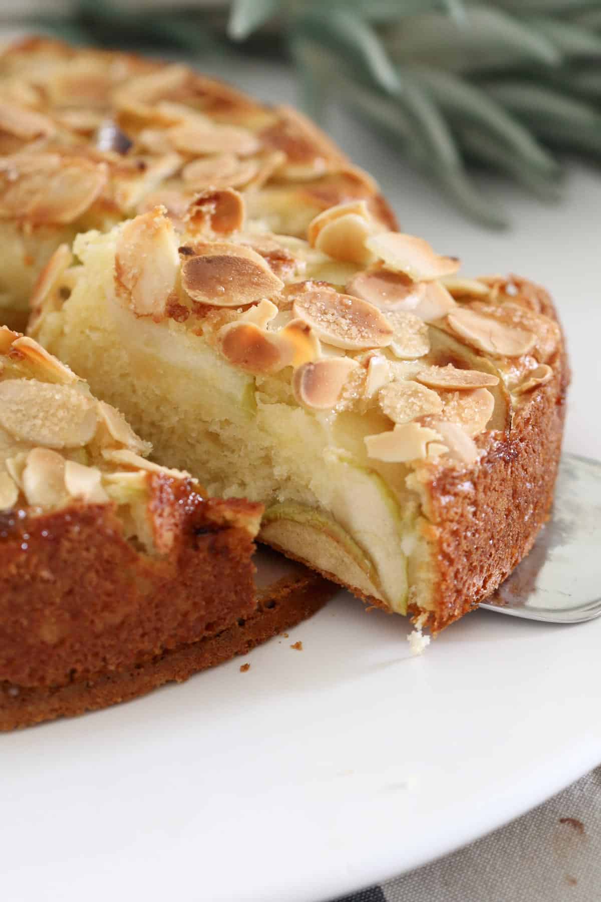 A piece of apple cake with almonds on top being removed from the entire cake.