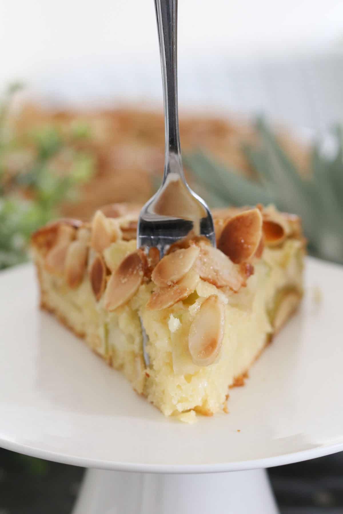 A fork in a slice of elegant almond cake served on a cake stand.