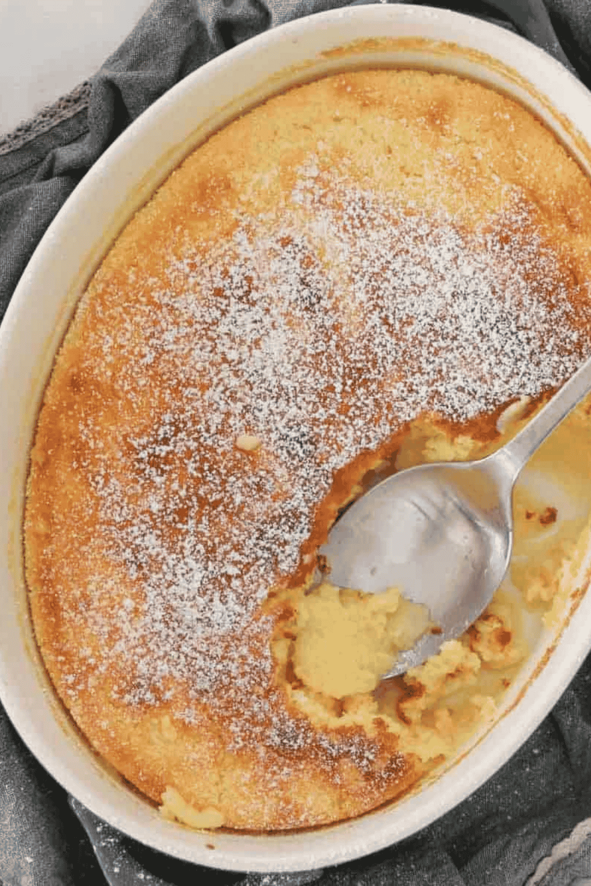 An overhead shot of a lemon delicious pudding sprinkled with icing sugar.