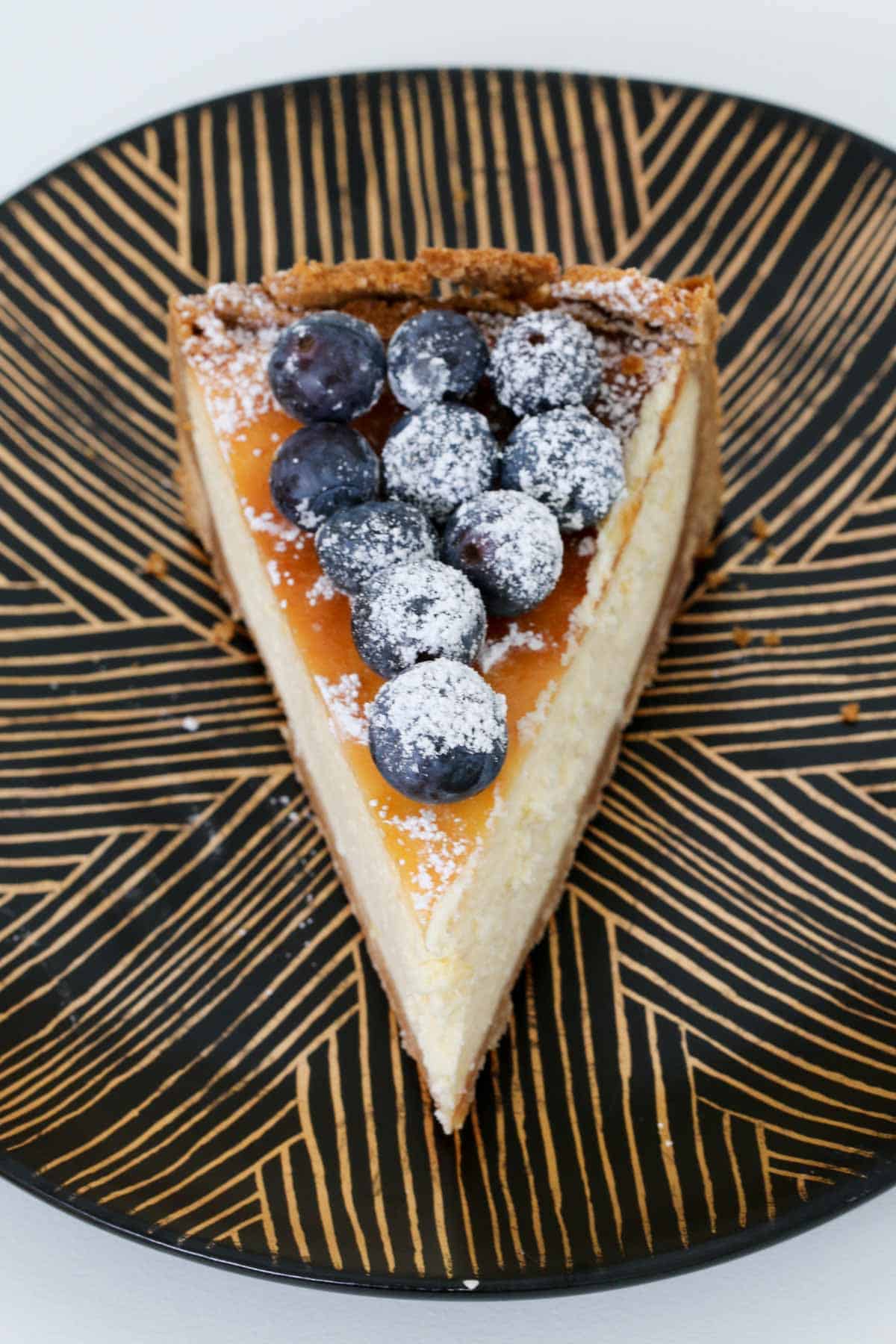 An overhead shot of a piece of baked cheesecake with blueberries on top.