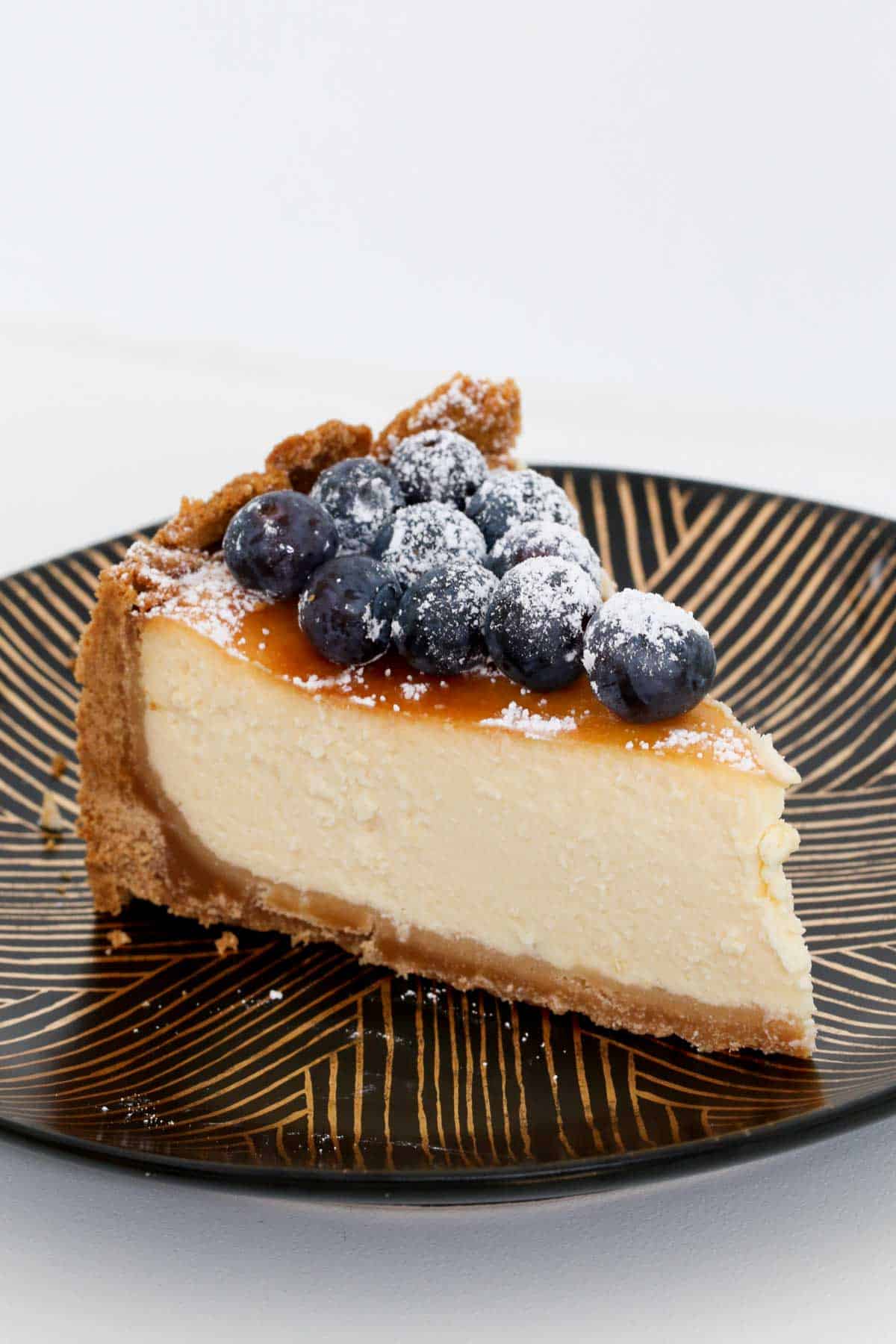 A piece of creamy cheesecake dessert on a black and gold plate.